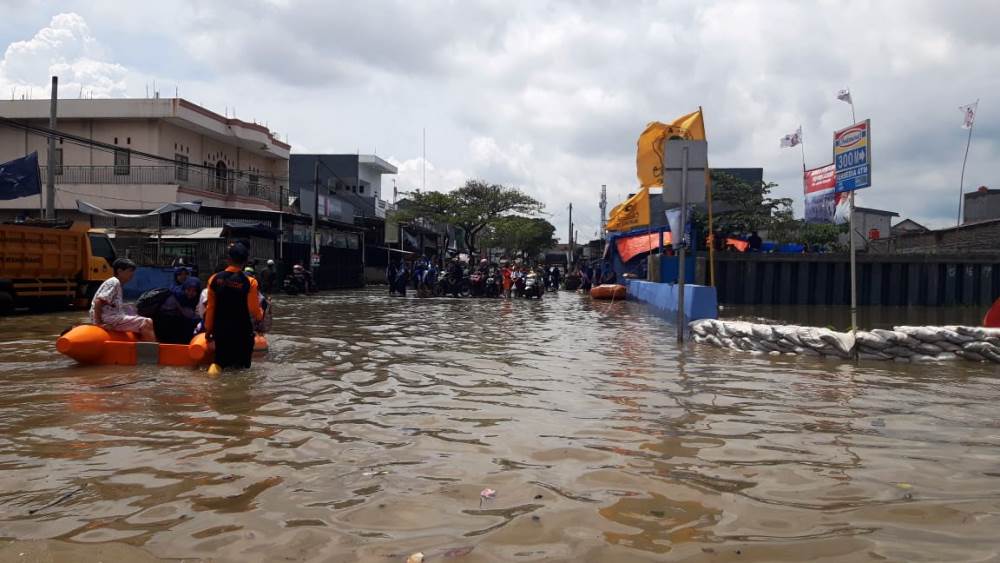 Petugas BPBD Kota Tangerang membantu masyarakat yang ingin menyebrang melewati akses Jalan Regency yang banjir di Kecamatan Periuk, Kota Tangerang.