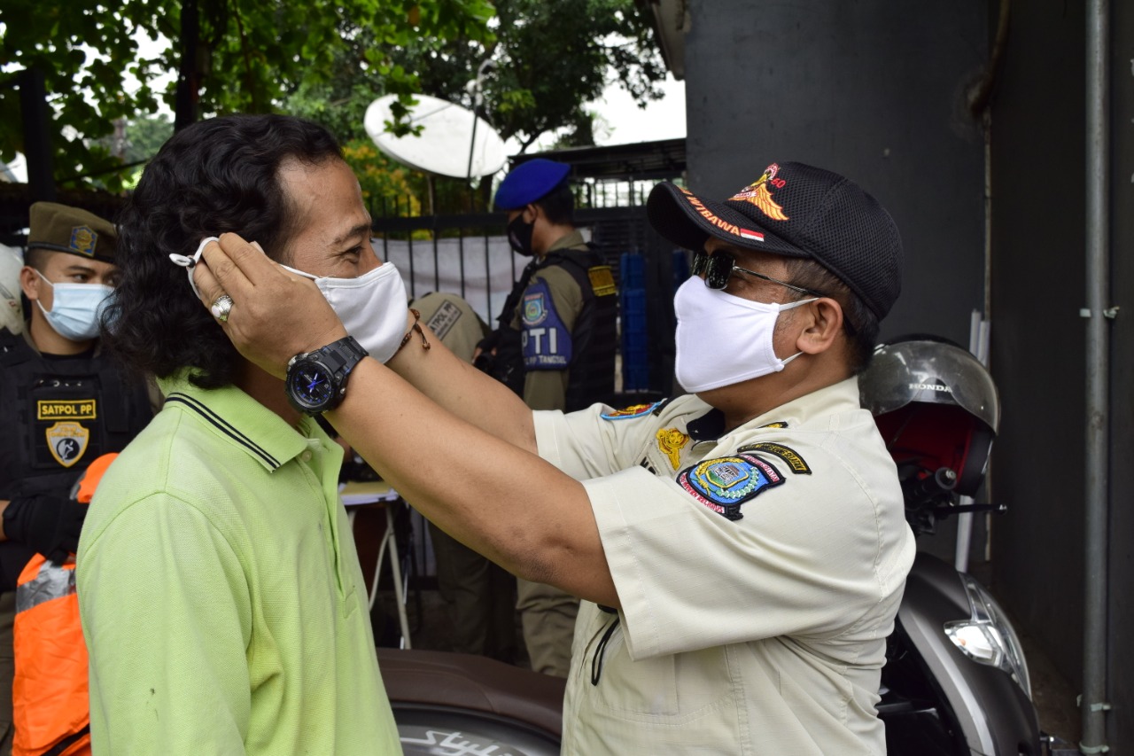 Personel Satuan Polisi Pamong Praja (Satpol PP) Kota Tangerang Selatan saat memakaikan masker kepada masyarakat setempat, Tangerang Selatan, Rabu (4/11/2020).